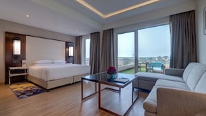 A modern hotel room with a large bed, a sofa, a coffee table, and a balcony with a view. - Courtyard by Marriott Surat (Surat)