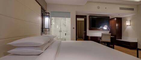 A hotel room with a large bed, a desk, a chair, a mirror, and a shower area.