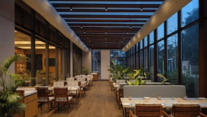 A restaurant with a long counter, wooden chairs, and large windows. - Courtyard by Marriott Surat (Surat)