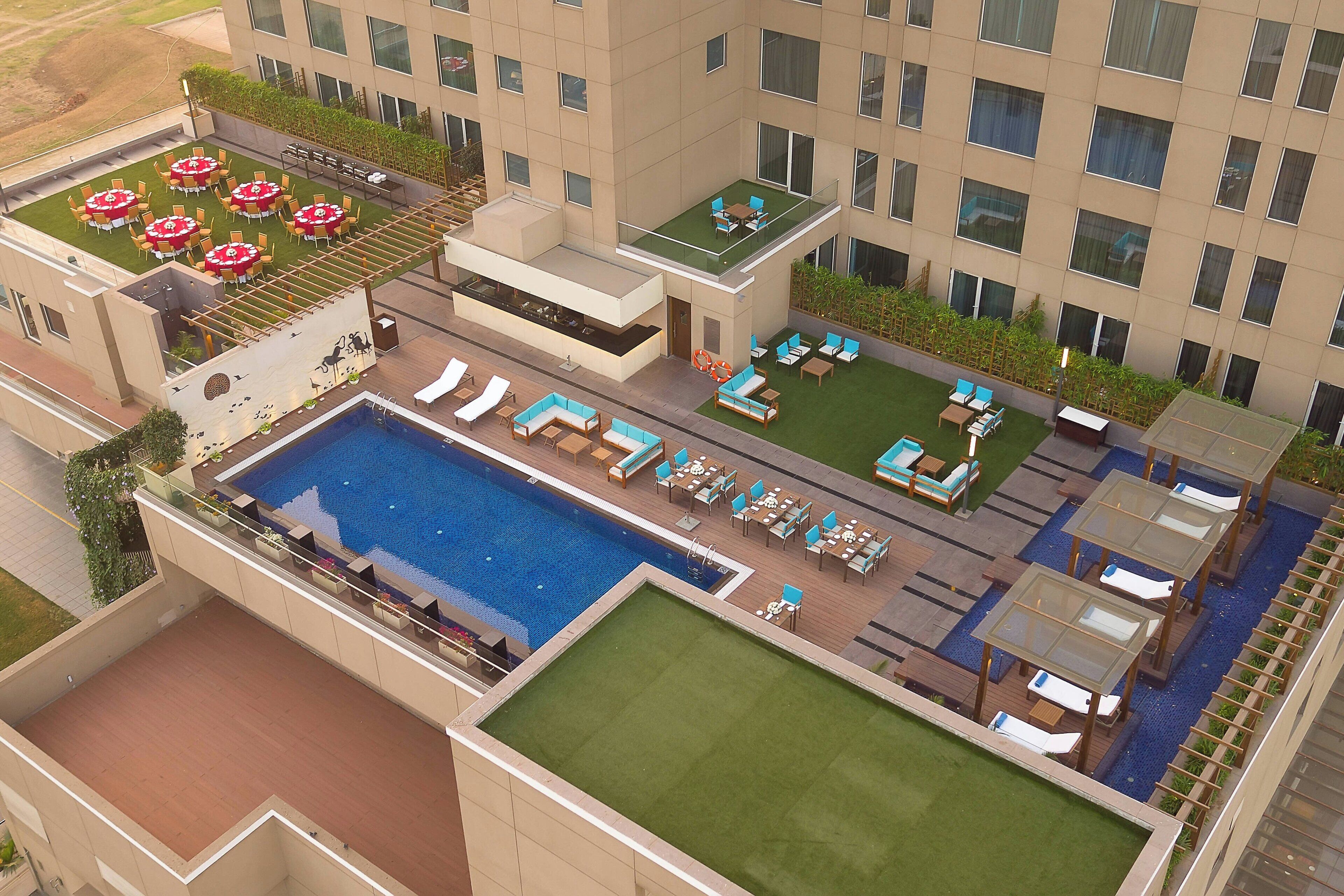 A rooftop pool area with multiple seating areas, a large pool, and a green lawn.