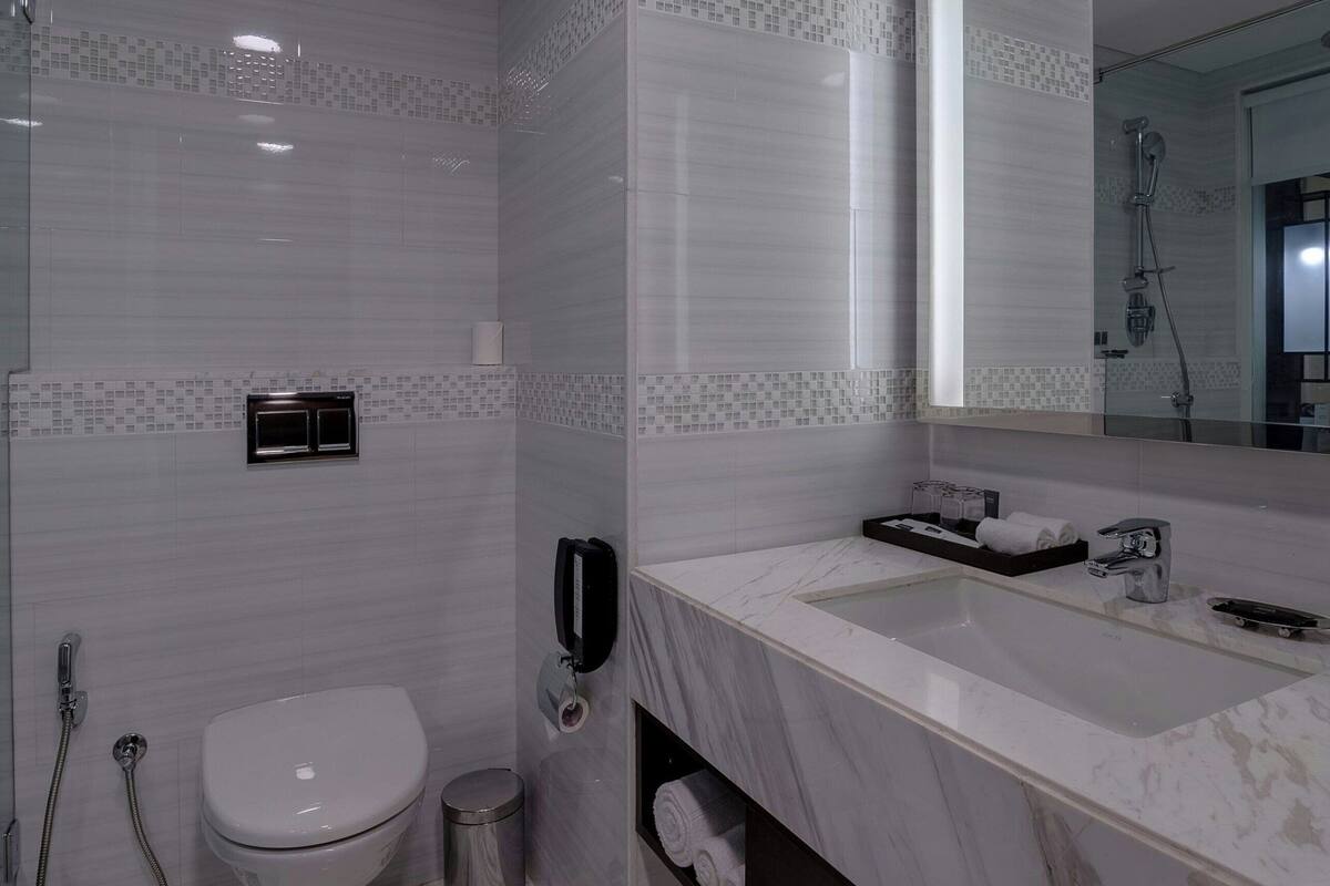 A modern bathroom with a large mirror, a white toilet, a sink with a marble countertop, and a shower area.