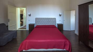 A bedroom with a large bed, a wardrobe, a bedside table, a lamp, and a door leading to another room.