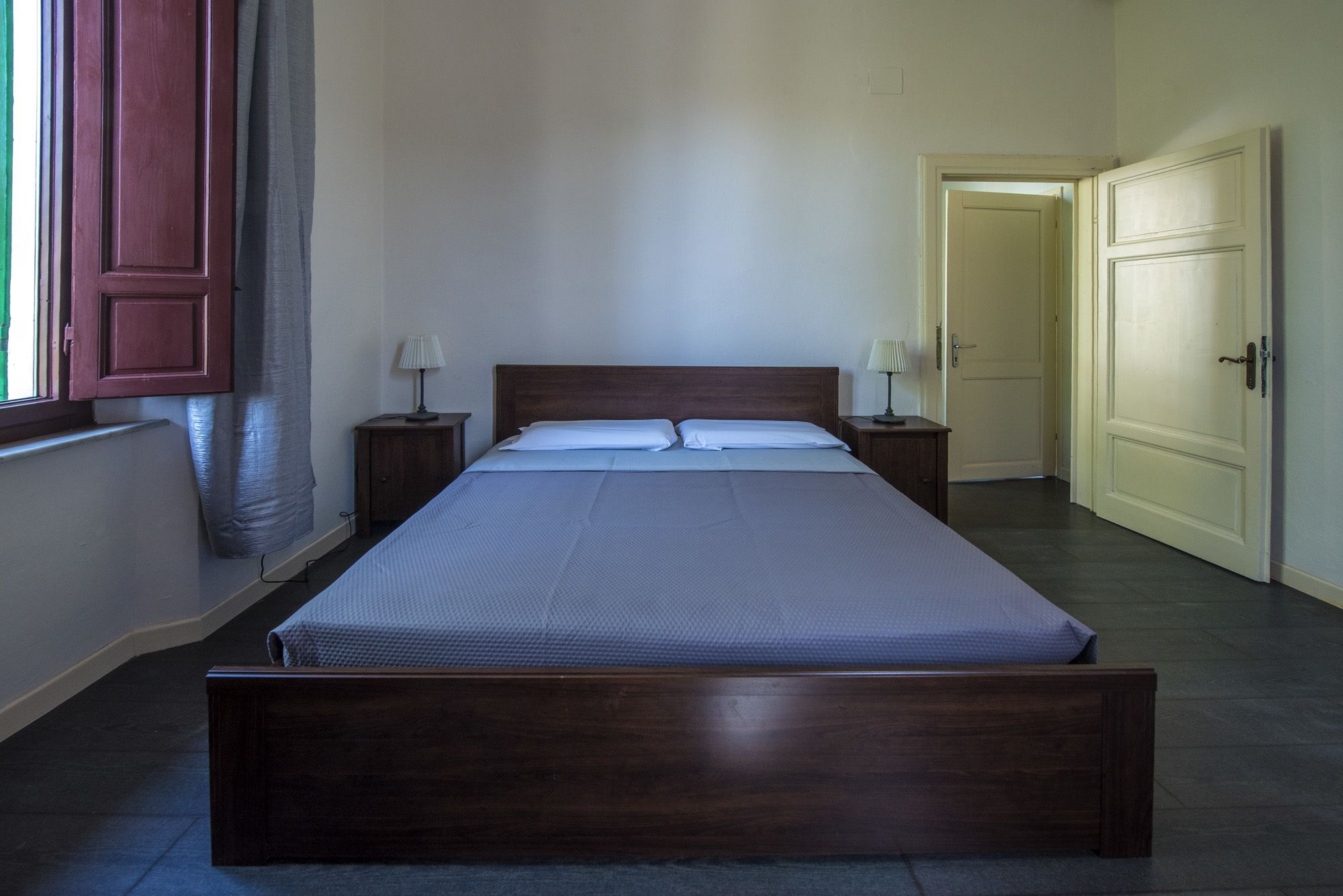 A standard single bed in a hotel room with a wooden headboard, two bedside tables with lamps, and a plain white wall.