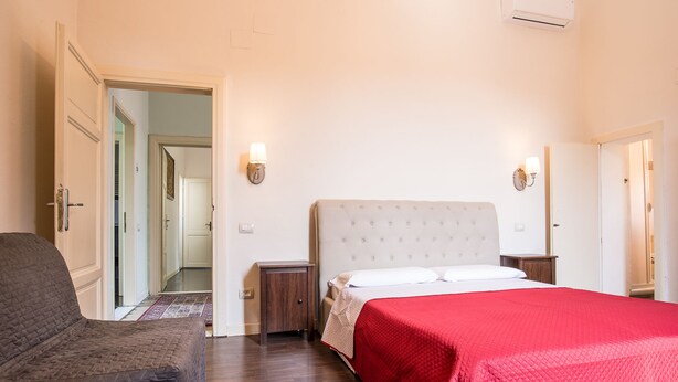 A bedroom with a bed, a nightstand, a chair, and a door leading to another room. - Villa Regina (Pisa)