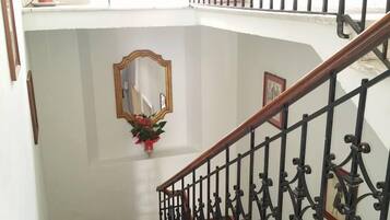 Uma escadaria com corrimão em ferro preto, um espelho e um vaso com flores na parede.