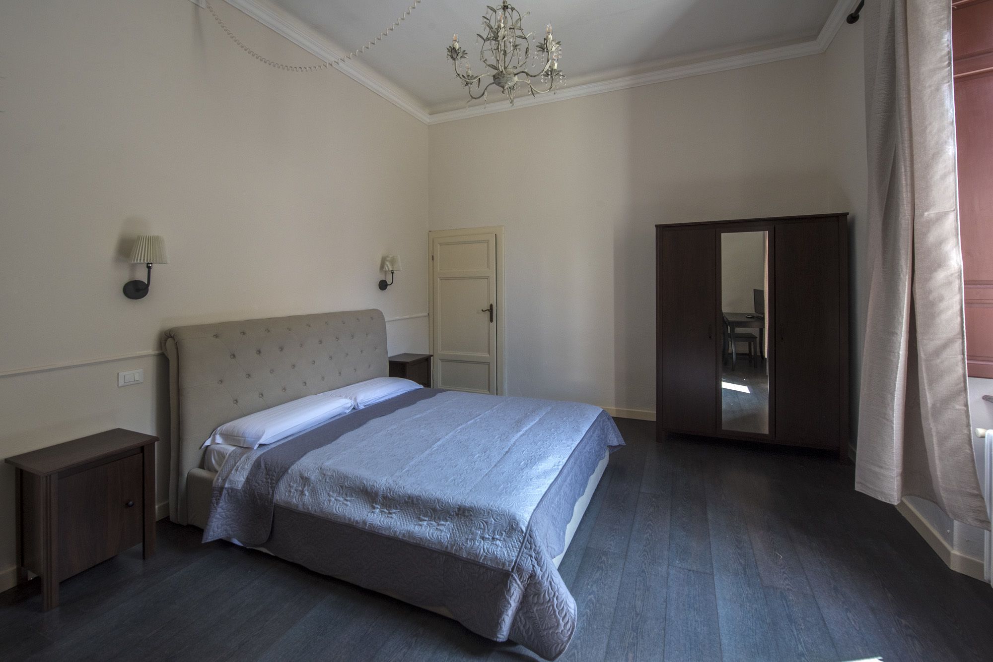 Un dormitorio con cama, mesitas de noche, armario, lámpara de araña y una puerta.