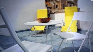 A terrace with a white table and yellow chairs, a bowl of fruit on the table, and a view of a historic building in the background. - Sciacca B&B Natoli (Sciacca)