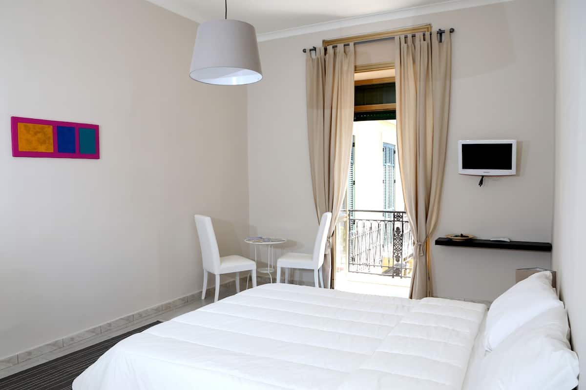 A hotel room with a bed, a chair, a small table, a TV, and a window with curtains.
