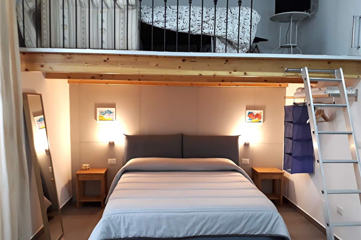 A compact bedroom with a bunk bed, bedside lamps, a ladder, and artwork on the walls.