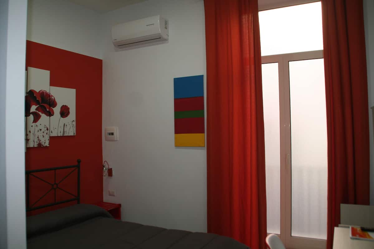 A bedroom with a bed, a red curtain, a window, and wall art.