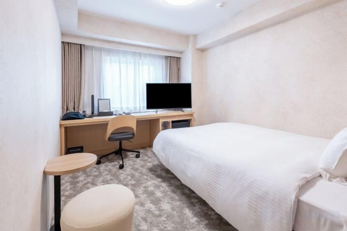 A hotel room with a bed, a desk with a computer, a chair, and a television.