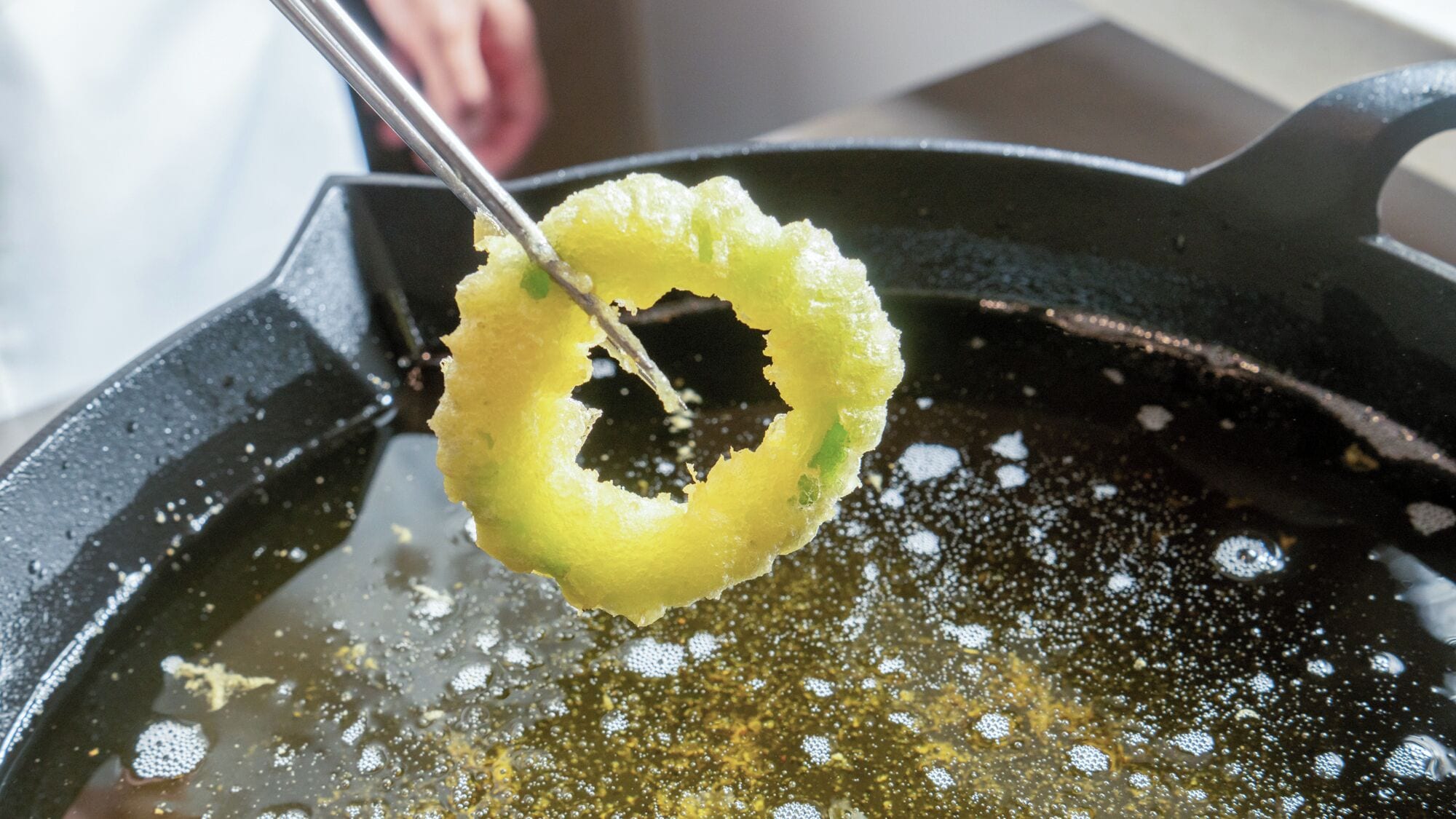 A frying pan with oil and a partially cooked dough ring.