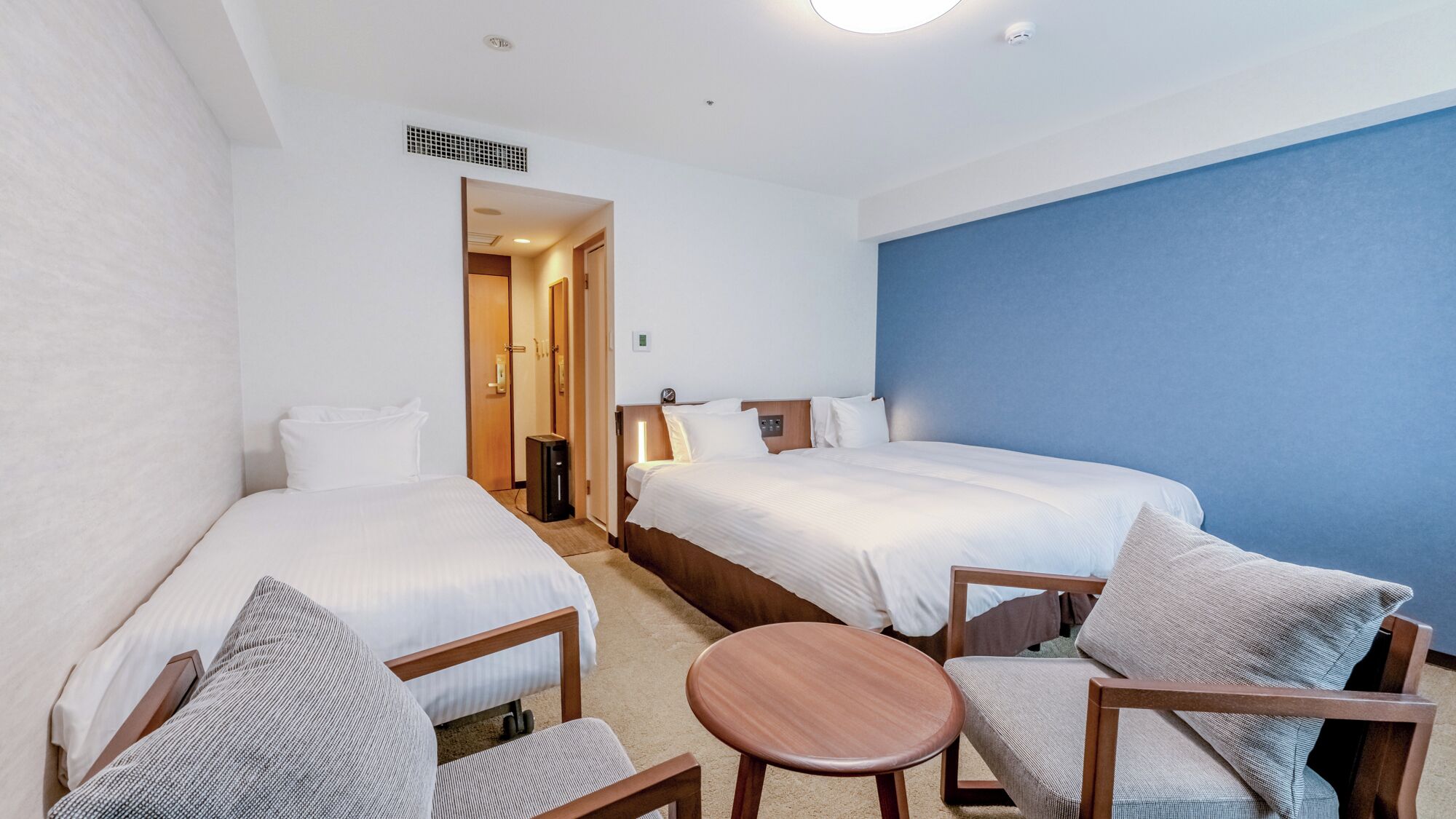 Quarto de hotel com duas camas, uma mesa redonda pequena e uma cadeira.
