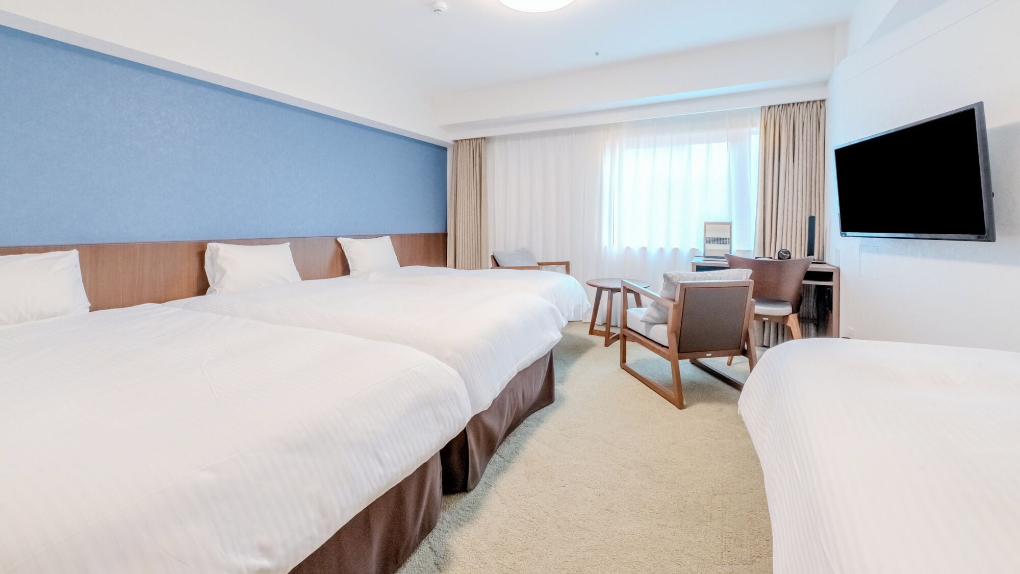 Habitación de hotel con dos camas, un escritorio, una silla, un televisor y una ventana con cortinas.