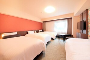 Hotellihuone, jossa on kolme sänkyä, pieni pöytä, televisio ja ikkuna, jossa on verhot.
