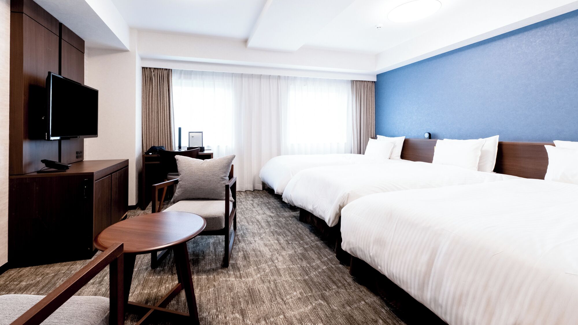 Habitación de hotel con cama, escritorio con televisor, una silla y una mesita.