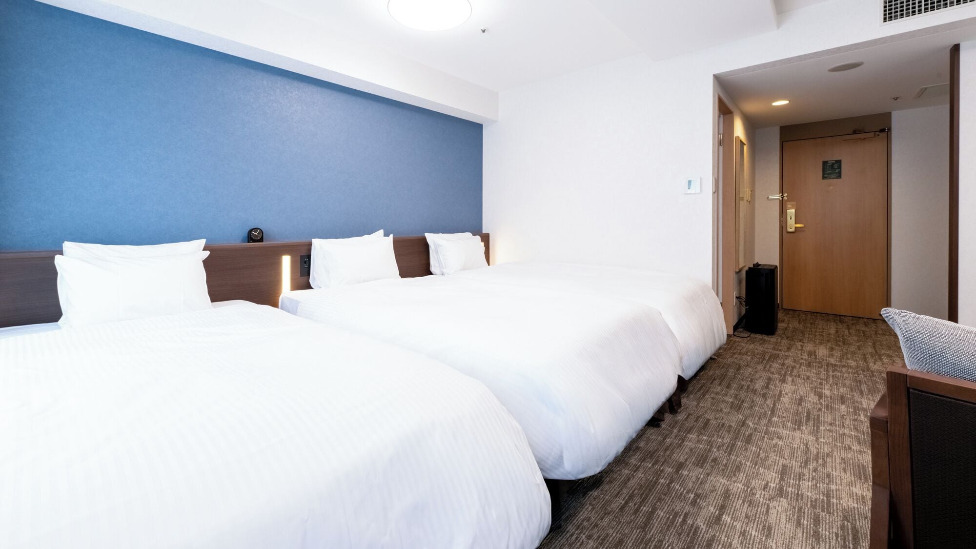 Ein Hotelzimmer mit zwei Betten, einer blauen Akzentwand, einem Holzkopfteil und einem Teppichboden.