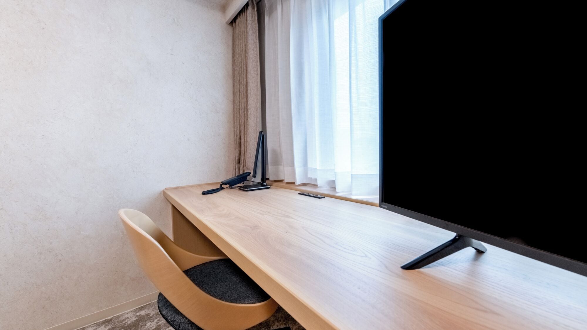 A room with a wooden desk, a chair, a standing lamp, and a television.
