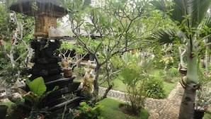 A garden with a stone structure, a thatched roof, and various plants. - Pondok Indah Bungalow Bingin (Pecatu)