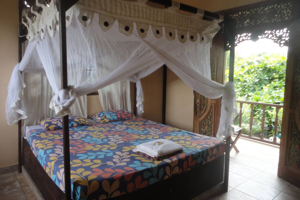 A bed with a colorful leaf-patterned bedspread, a white canopy, and a view of greenery outside.