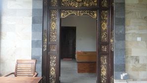 A wooden door with intricate carvings and a number '13' above it, leading into a room with a bed and a wooden chair. - Pondok Indah Bungalow Bingin (Pecatu)