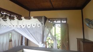A room with a wooden ceiling, a bed with a white canopy, a window with curtains, and a wall-mounted fan. - Pondok Indah Bungalow Bingin (Pecatu)