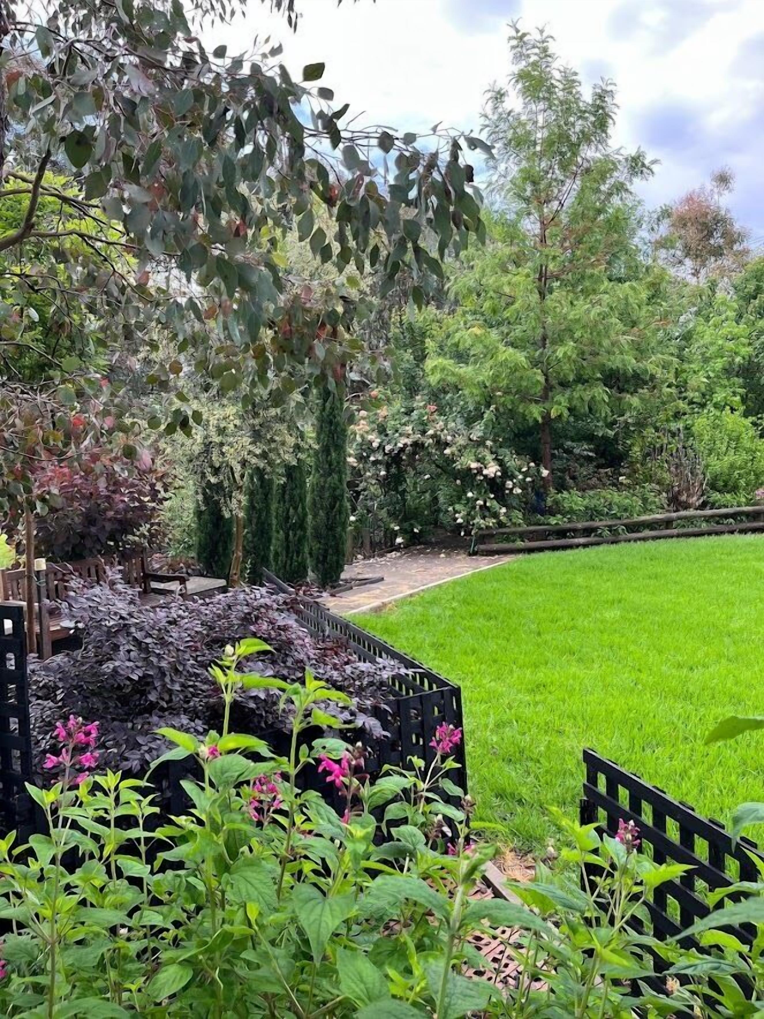 A well-maintained garden with a variety of plants and trees, a neatly trimmed lawn, and a wooden fence.