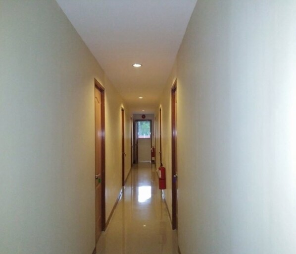 A narrow, well-lit hallway with wooden doors on either side, leading to a room with a window.