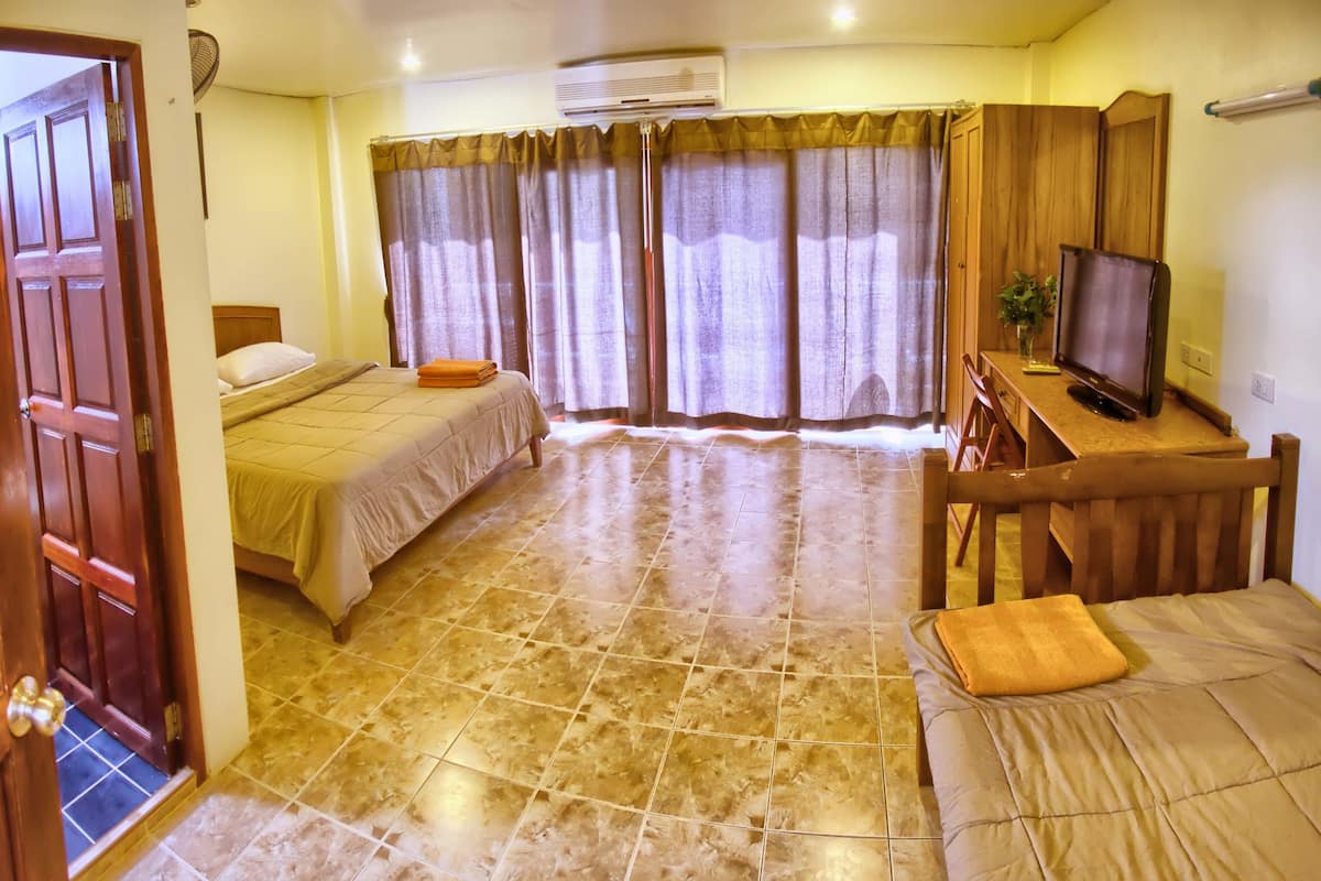 A hotel room with two beds, a TV, a desk, and a large window with curtains.