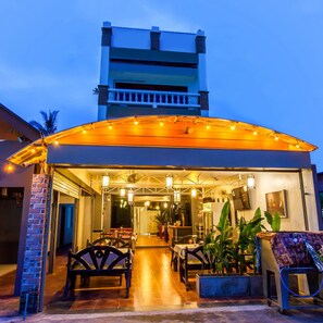 A restaurant with outdoor seating, a covered patio, and a view of a tall building in the background. - Hugs Guesthouse (Ko Lanta)