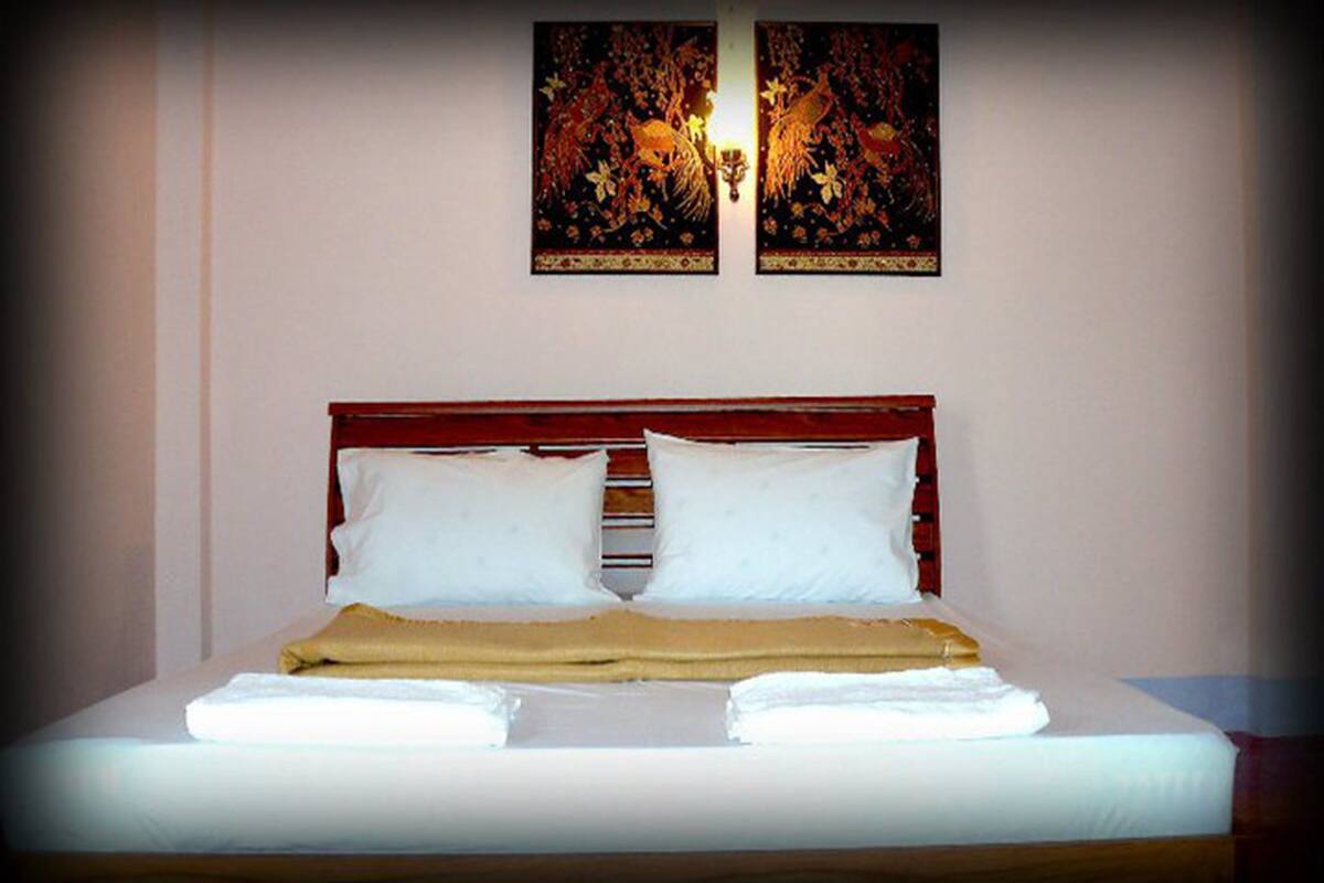 A neatly made bed with white linens and a brown blanket, a wooden headboard, and two wall-mounted artworks above.