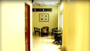 A narrow hallway with a wooden door on the left, a ceiling fan, and a framed picture on the wall. There are two chairs and a small table in the room. - D's Corner & Guesthouse (Phuket)