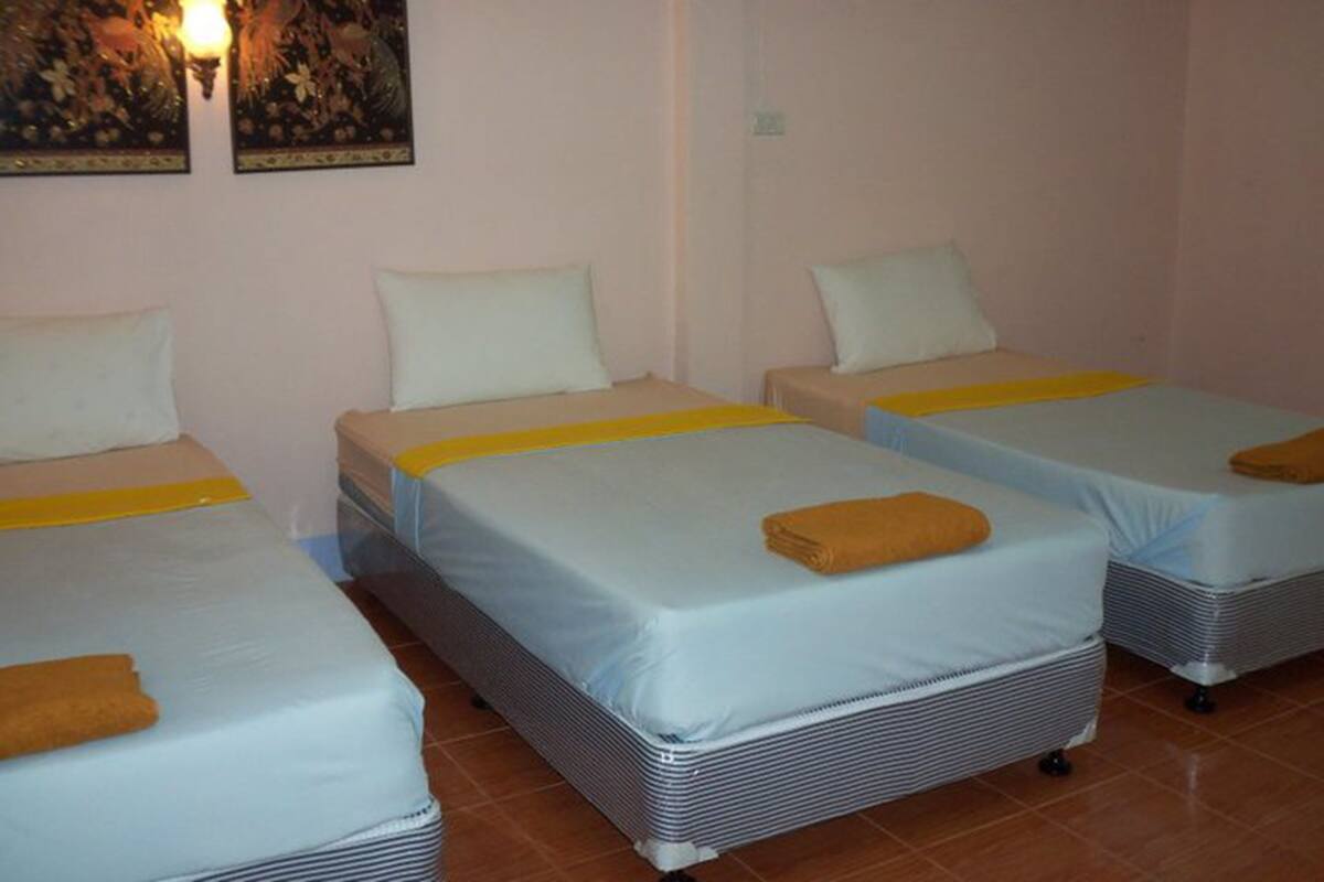 A hotel room with three single beds, each with a yellow-striped bedspread and white pillows.