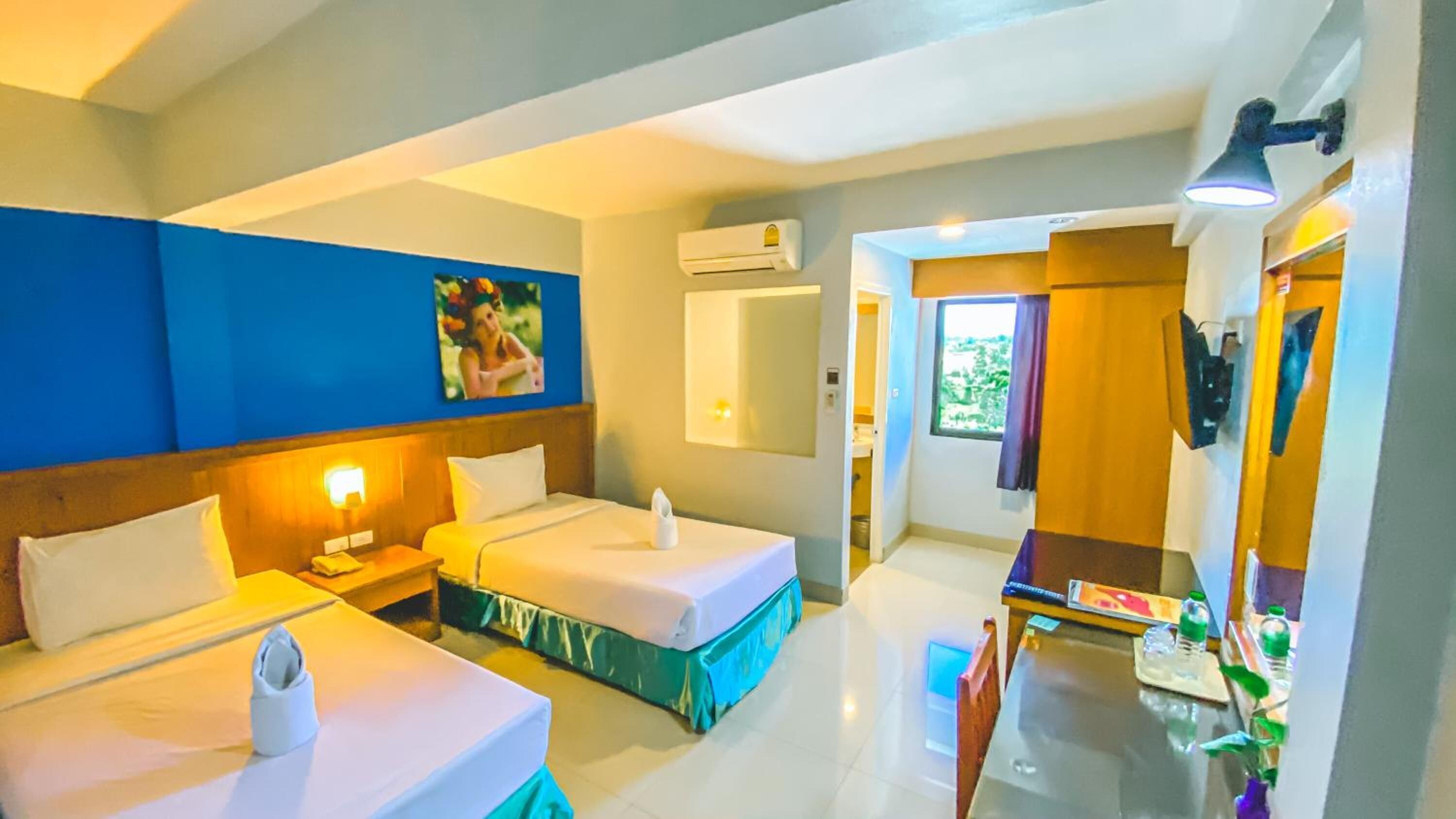 Une chambre d’hôtel avec deux lits, un bureau, une chaise, un miroir et un appareil de climatisation.