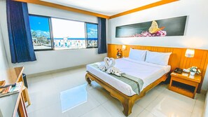 Habitación de hotel con cama, escritorio, silla, ventana con vistas y un cuadro en la pared.
