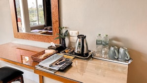 Ein Schreibtisch im Hotelzimmer mit Kaffeemaschine, Wasserflaschen, Wasserkocher, Fernbedienung und einer Zeitschrift.
