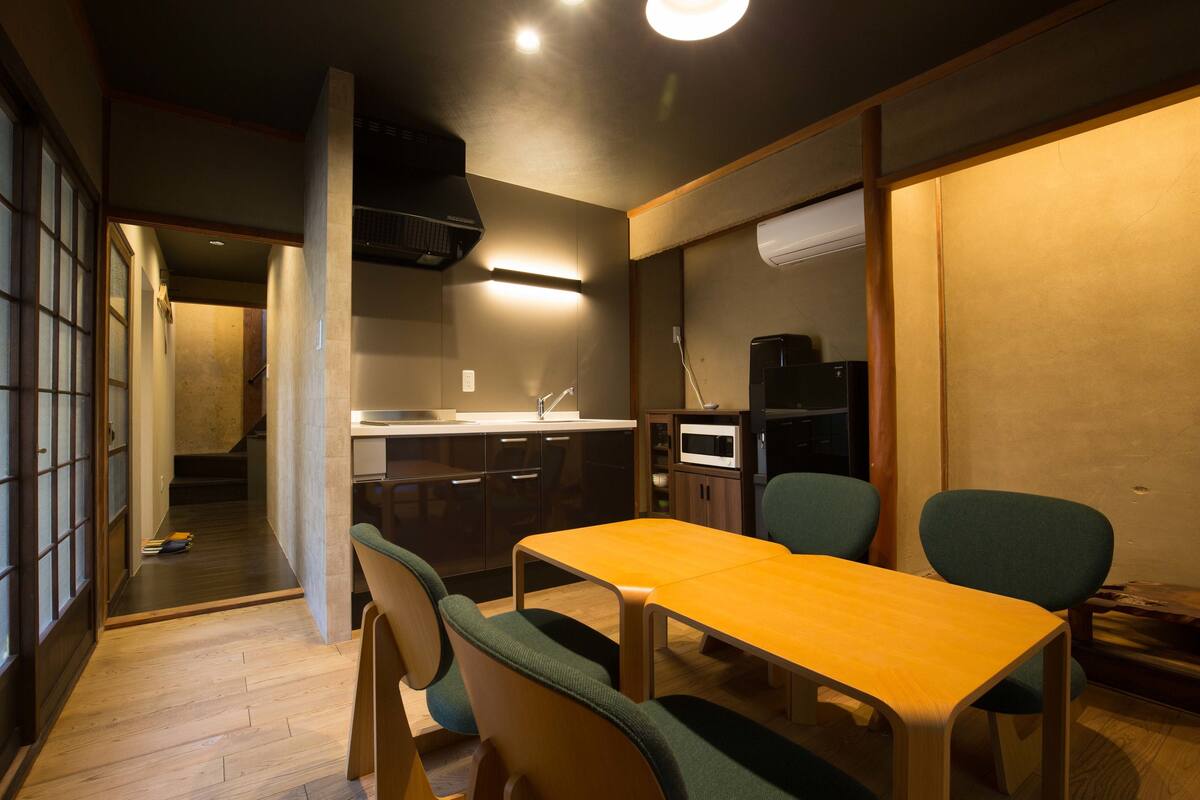 A compact kitchen with a microwave, sink, and cabinets. There is a dining table with chairs and a wooden floor.