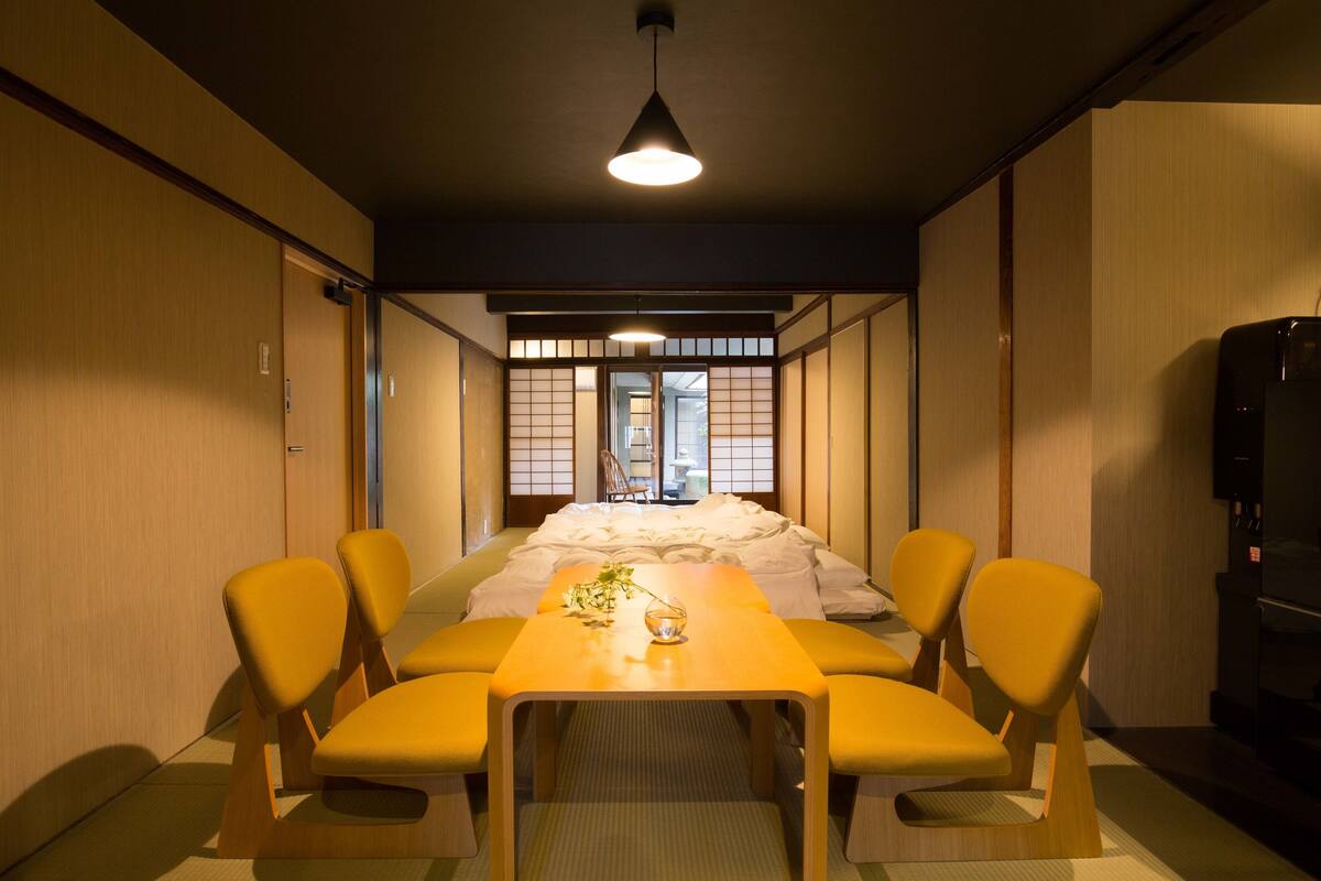 A traditional Japanese-style room with tatami flooring, a low table with cushions, and a sliding door leading to a bathroom.