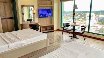Une chambre d’hôtel équipée d’un lit, d’un bureau, d’une télévision et d’une grande fenêtre donnant sur la ville.
