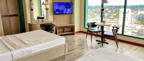 Habitación de hotel con cama, escritorio, televisión y un amplio ventanal con vista a la ciudad.