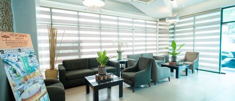 A modern hotel lobby with a reception desk, seating area, and large windows.