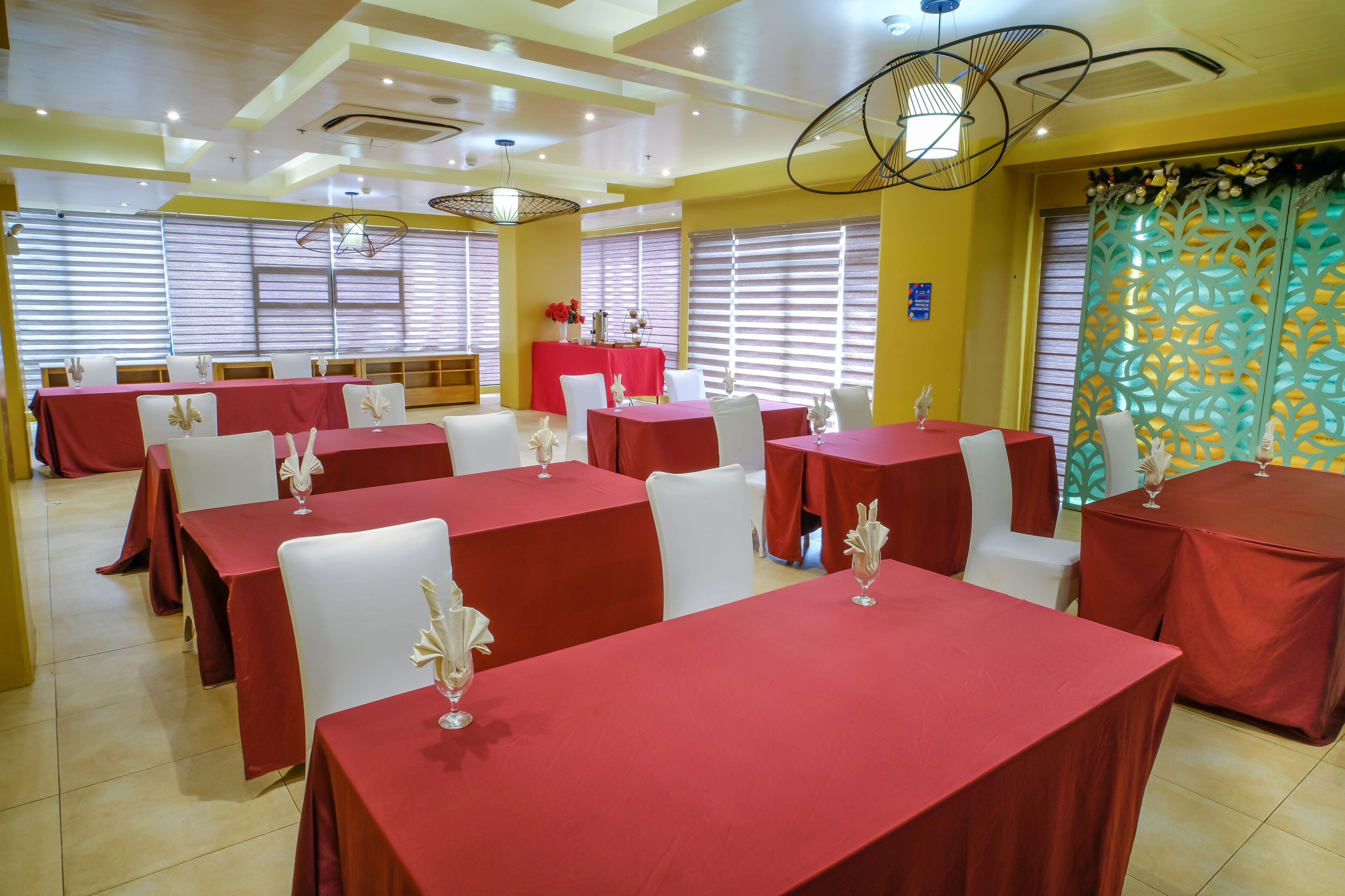 A dining area with multiple tables covered in red tablecloths, white chairs, and decorative glassware.