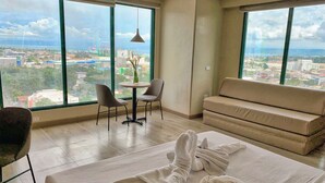 A hotel room with a large window, a sofa, a table with chairs, and a bed with towels. - New Dawn Hotel Plus (Cagayan de Oro)