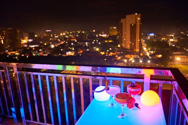 A balcony with a table featuring drinks and a glowing orb, overlooking a cityscape at night. - New Dawn Hotel Plus (Cagayan de Oro)