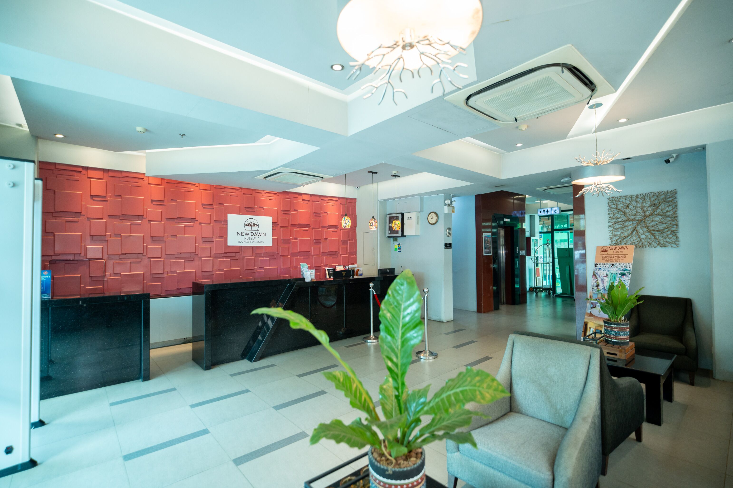 Zona de recepción de hotel con diseño moderno, que incluye un mostrador de recepción, un área de descanso y una planta decorativa.