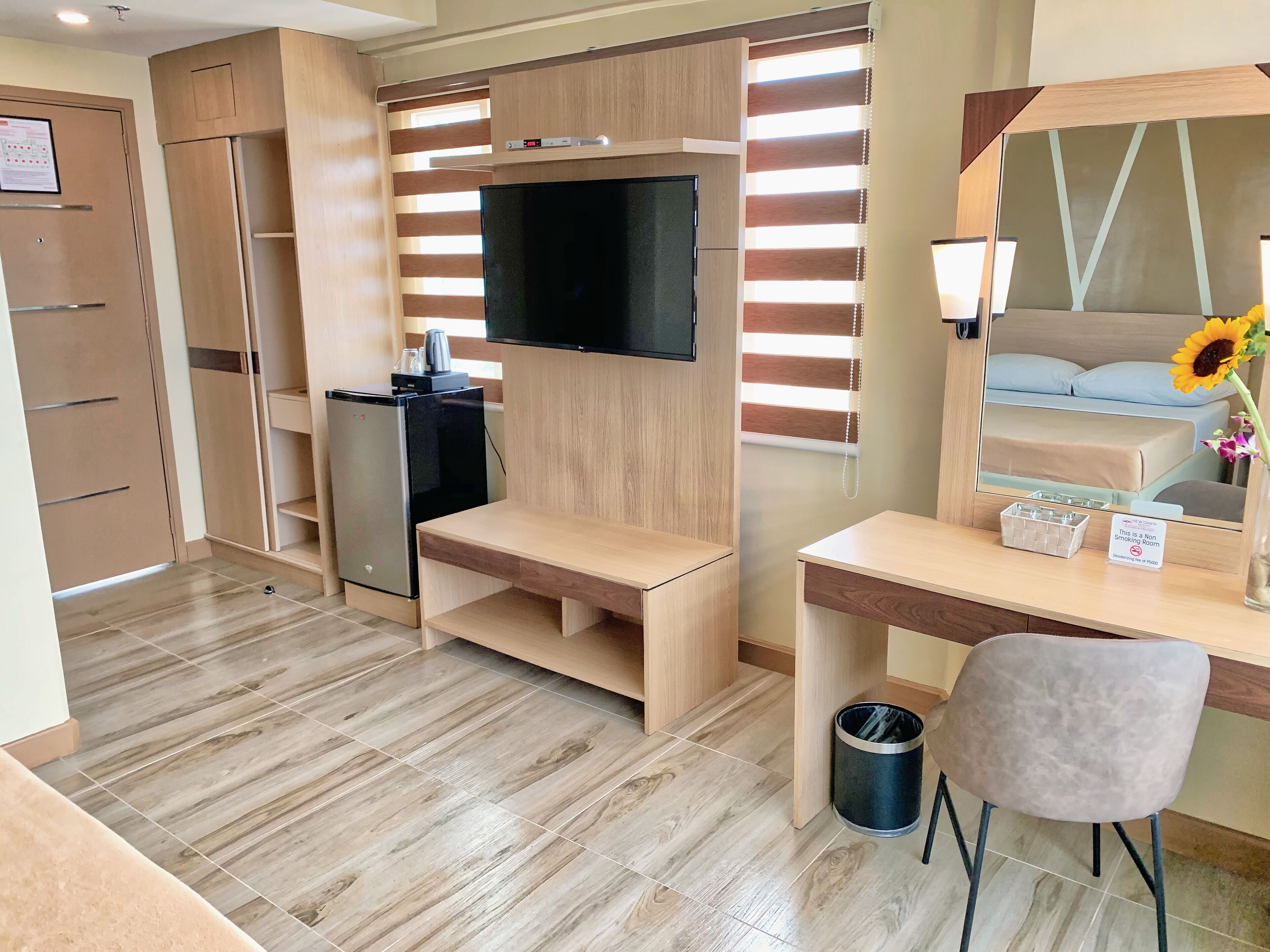 Habitación de hotel moderna con escritorio de madera, televisor de pantalla plana en la pared, refrigerador pequeño y un cubo de basura.
