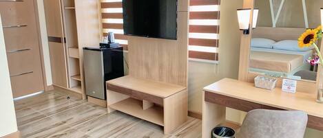 Habitación de hotel moderna con escritorio de madera, televisor de pantalla plana en la pared, refrigerador pequeño y un cubo de basura.