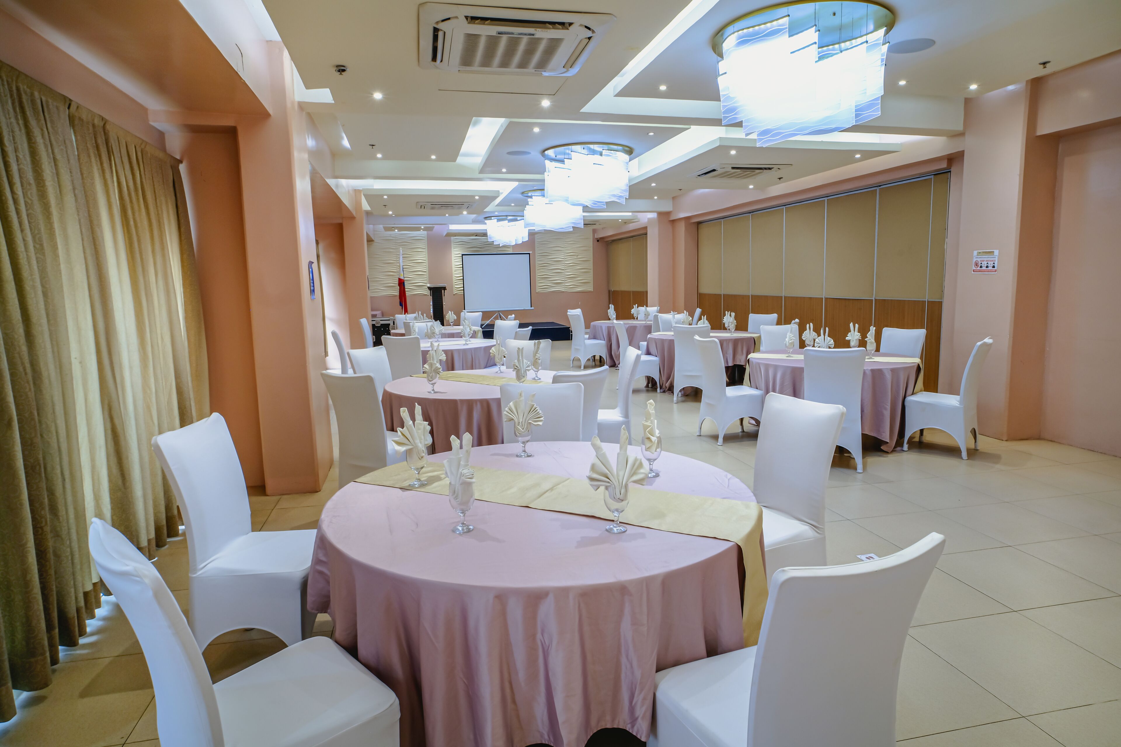 A banquet hall with round tables, white chairs, and a large screen.