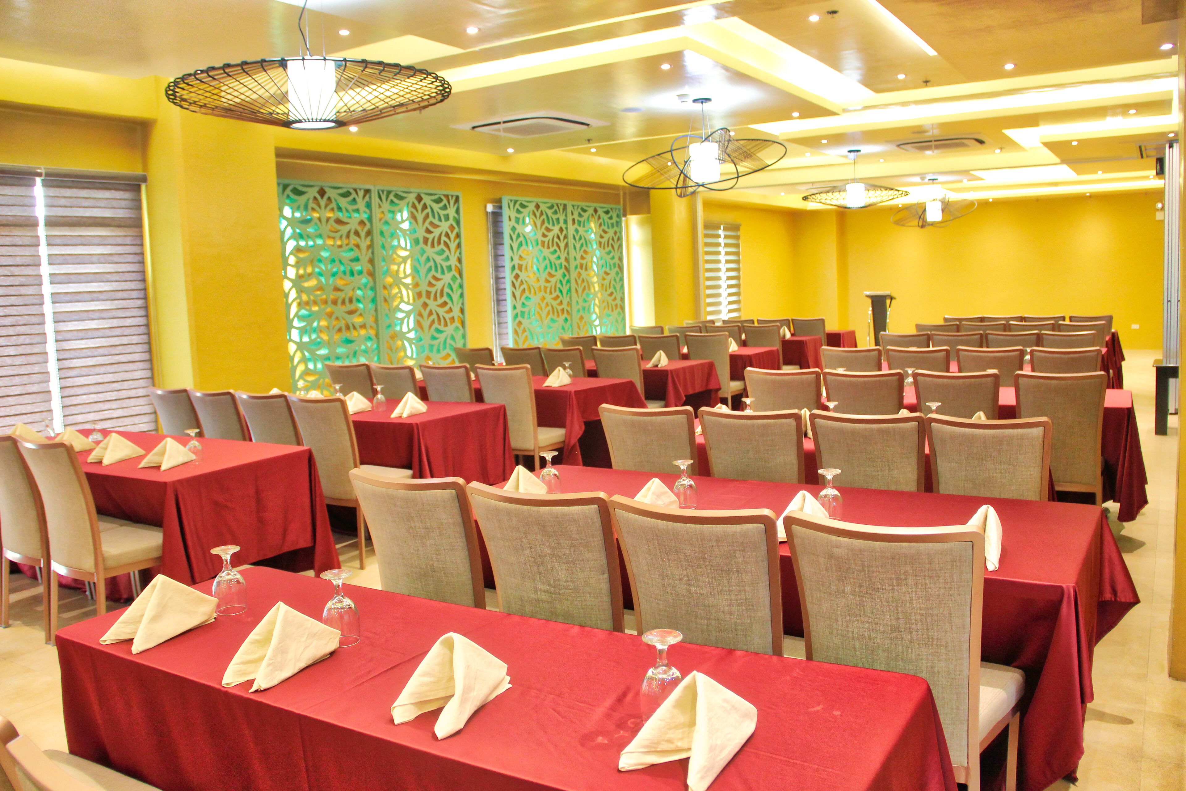 A conference room with multiple tables and chairs, red tablecloths, and a decorative ceiling design.
