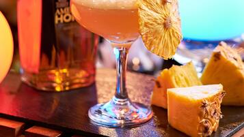 A bar setting with a cocktail glass, a bottle of liquor, and pineapple slices on a wooden bar counter.